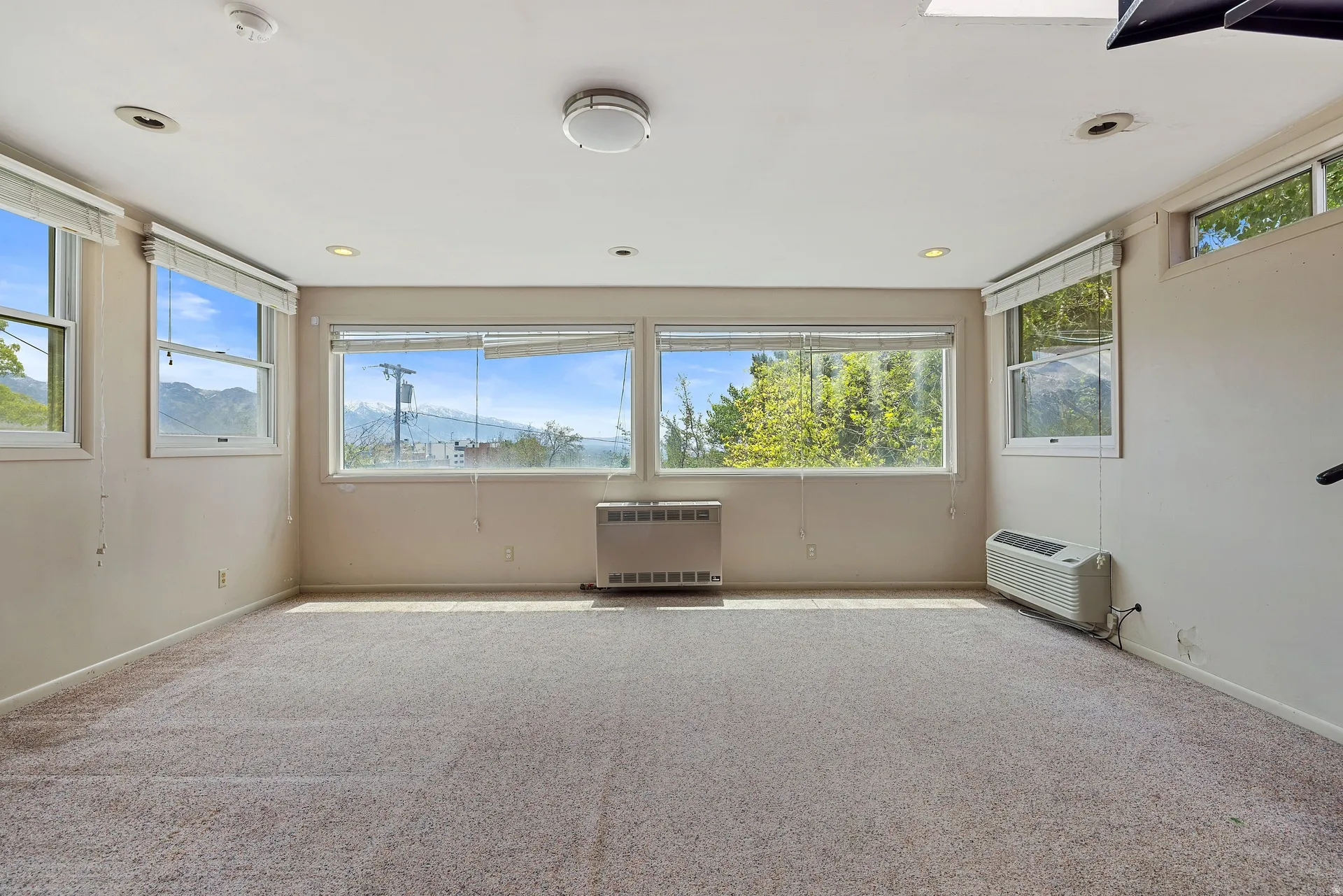 Carpeted room with multiple windows, recessed lighting, and wall-mounted heating/cooling units