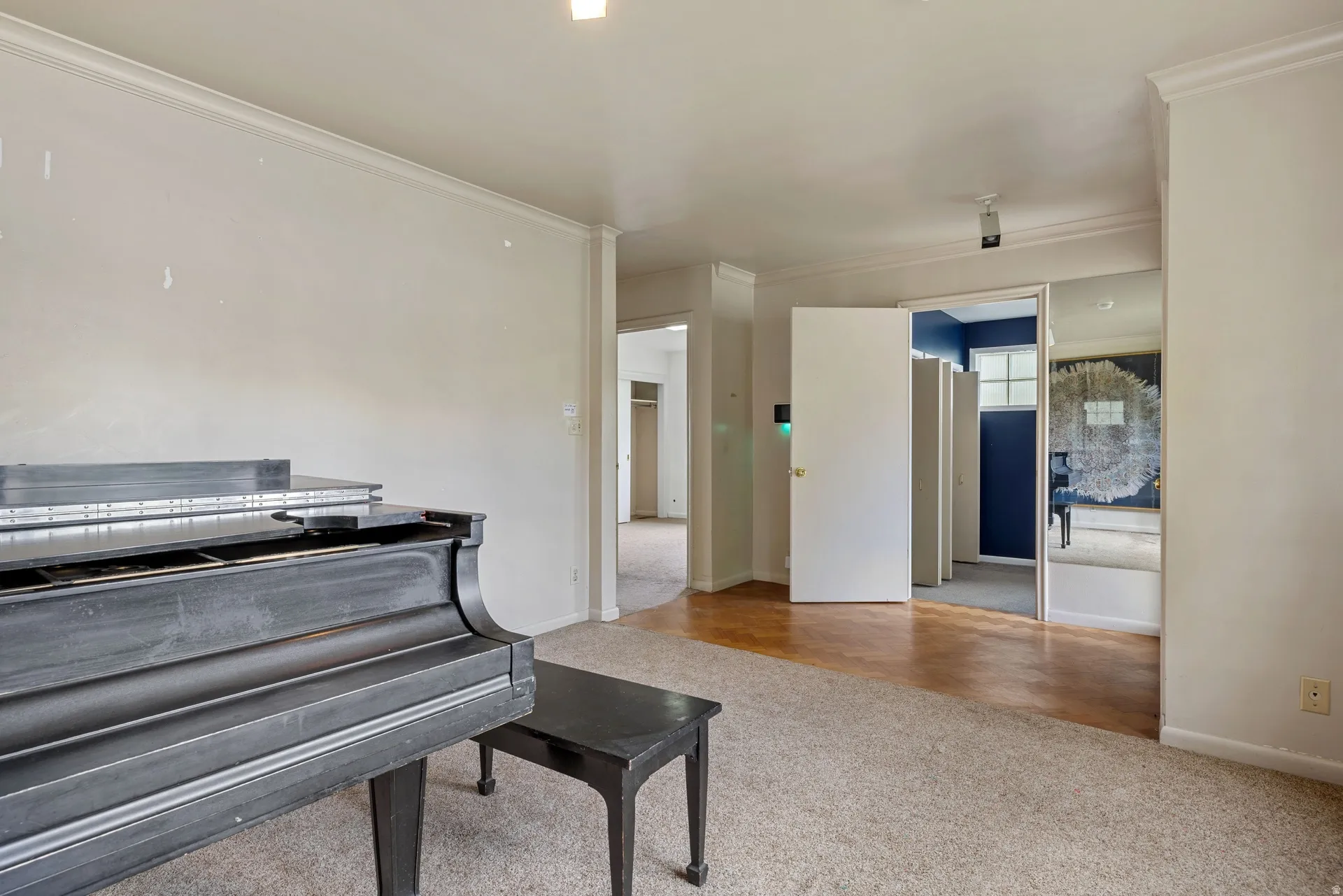 Spacious interior room featuring crown molding, neutral wall tones, and mixed flooring with carpeting and wood-finish sections