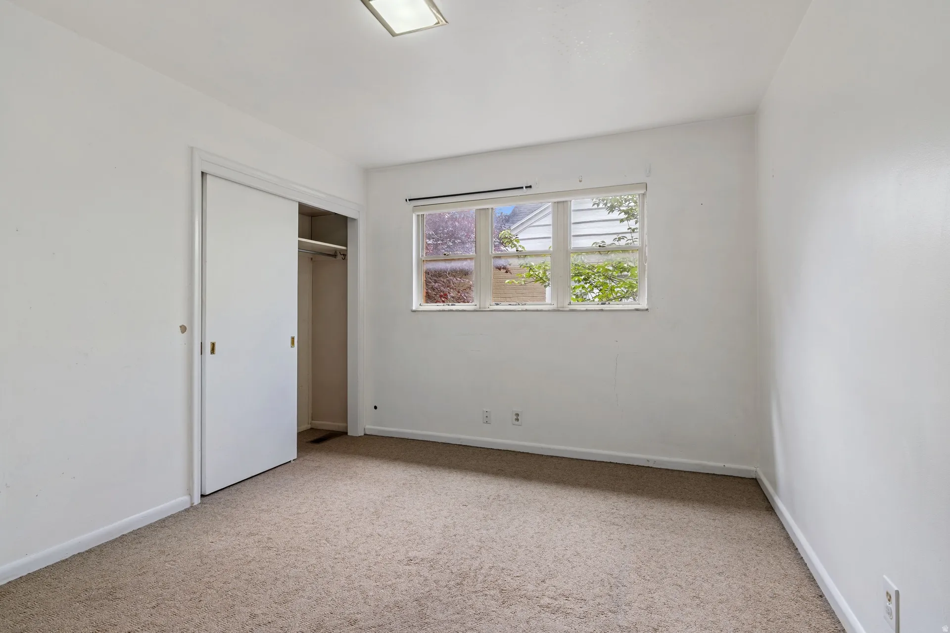 Carpeted room featuring a window with exterior views, white walls, and a built-in closet with sliding doors