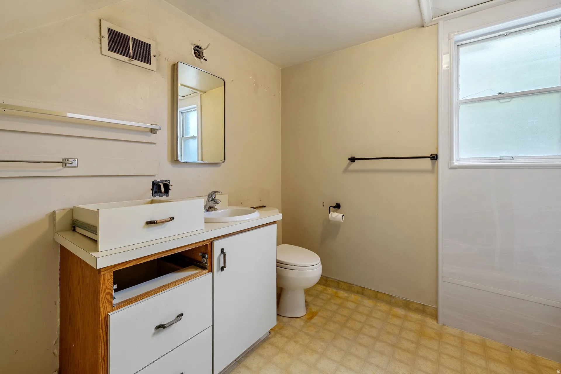Bathroom featuring a built-in vanity with a white countertop and wood-finish base, an integrated sink, a wall-mounted mirror, and a window with white trim