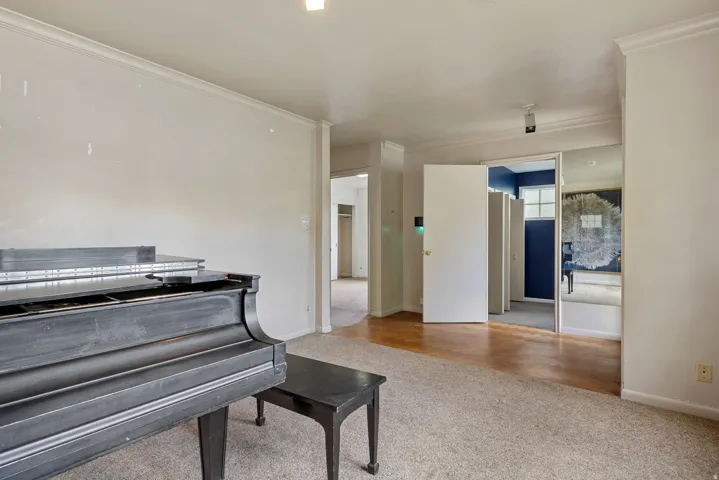 Spacious interior room featuring crown molding, neutral wall tones, and mixed flooring with carpeting and wood-finish sections