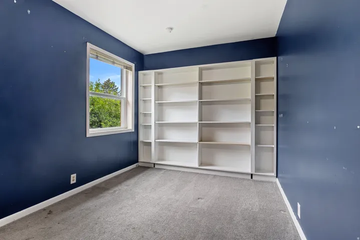 Room featuring a full wall of built-in shelving, a large window, and carpet flooring