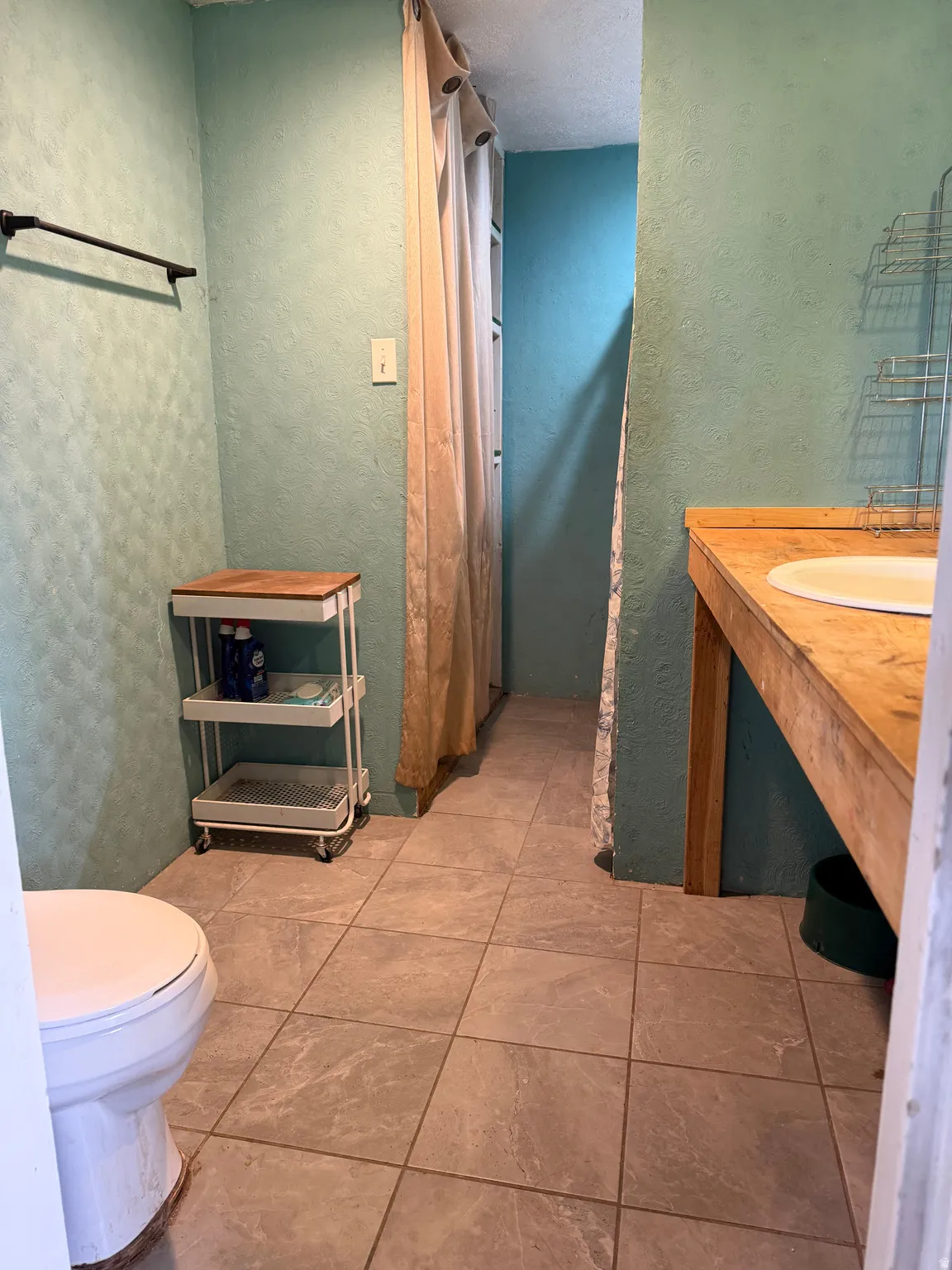 Bathroom featuring a toilet, tile flooring, a wood-finish vanity with an integrated sink, and a privacy curtain