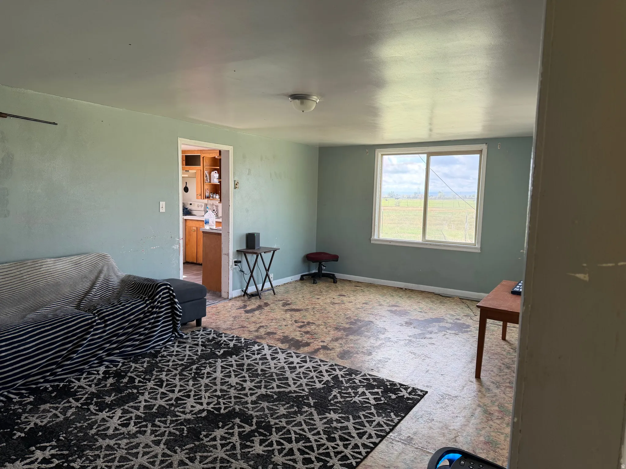 Room featuring a large window, light green wall paint, and a visible doorway to an additional space