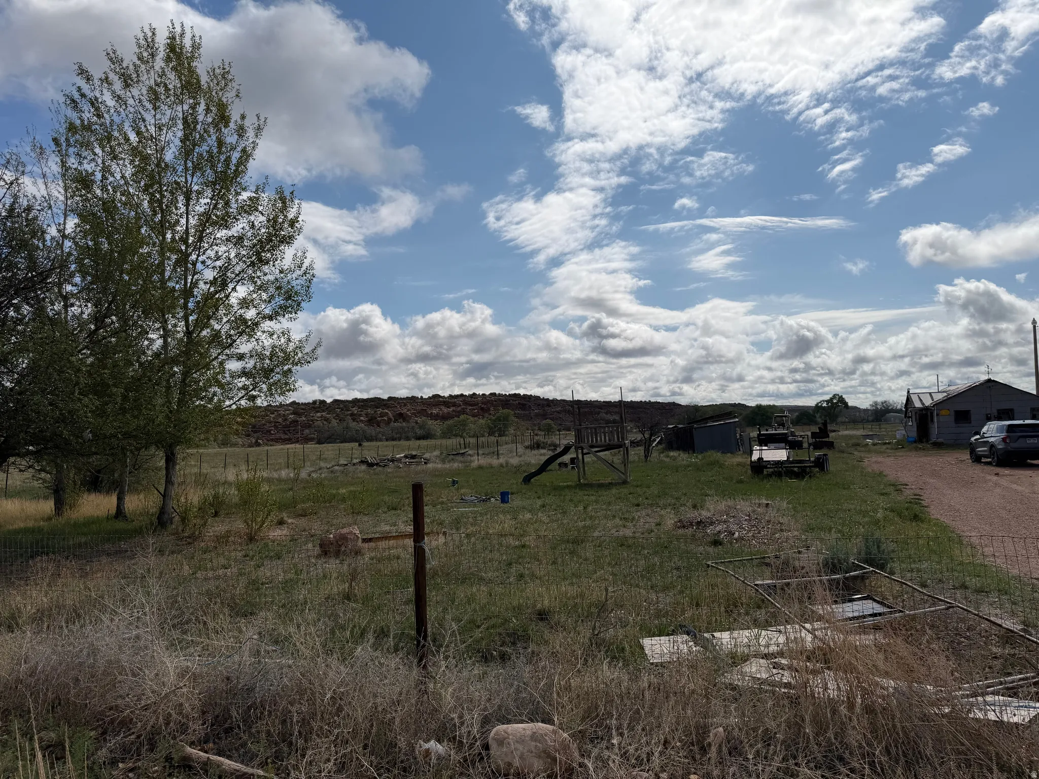 Rural landscape featuring expansive open space, distant hills, mature trees, and a gravel driveway leading to a structure