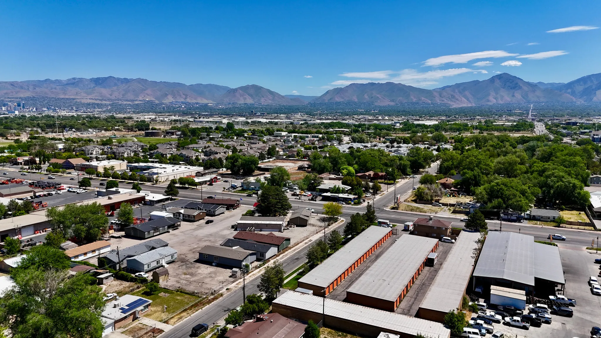 Expansive urban landscape featuring a clear blue sky, distant mountains, and a mixture of residential and commercial structures