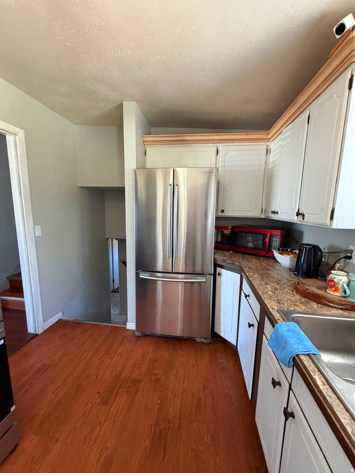 Kitchen with wood-finish flooring, stainless steel refrigerator, white cabinetry, and laminate countertops