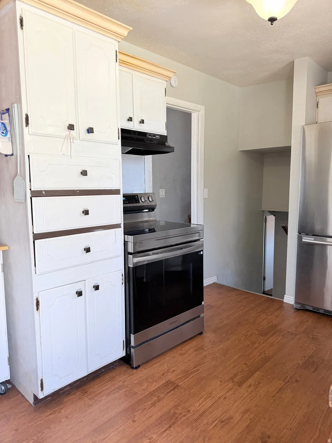 Kitchen featuring wood-finish flooring, white cabinetry, stainless steel range, and stainless steel refrigerator