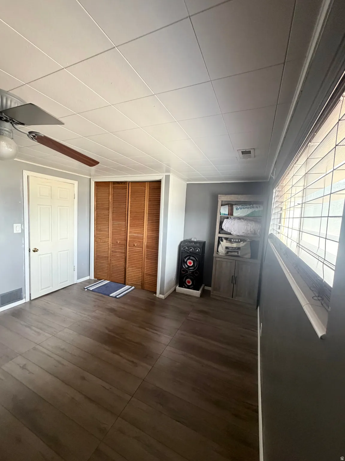Room with laminate wood-finish flooring, louvered bi-fold closet doors, white paneled door, and a ceiling fan
