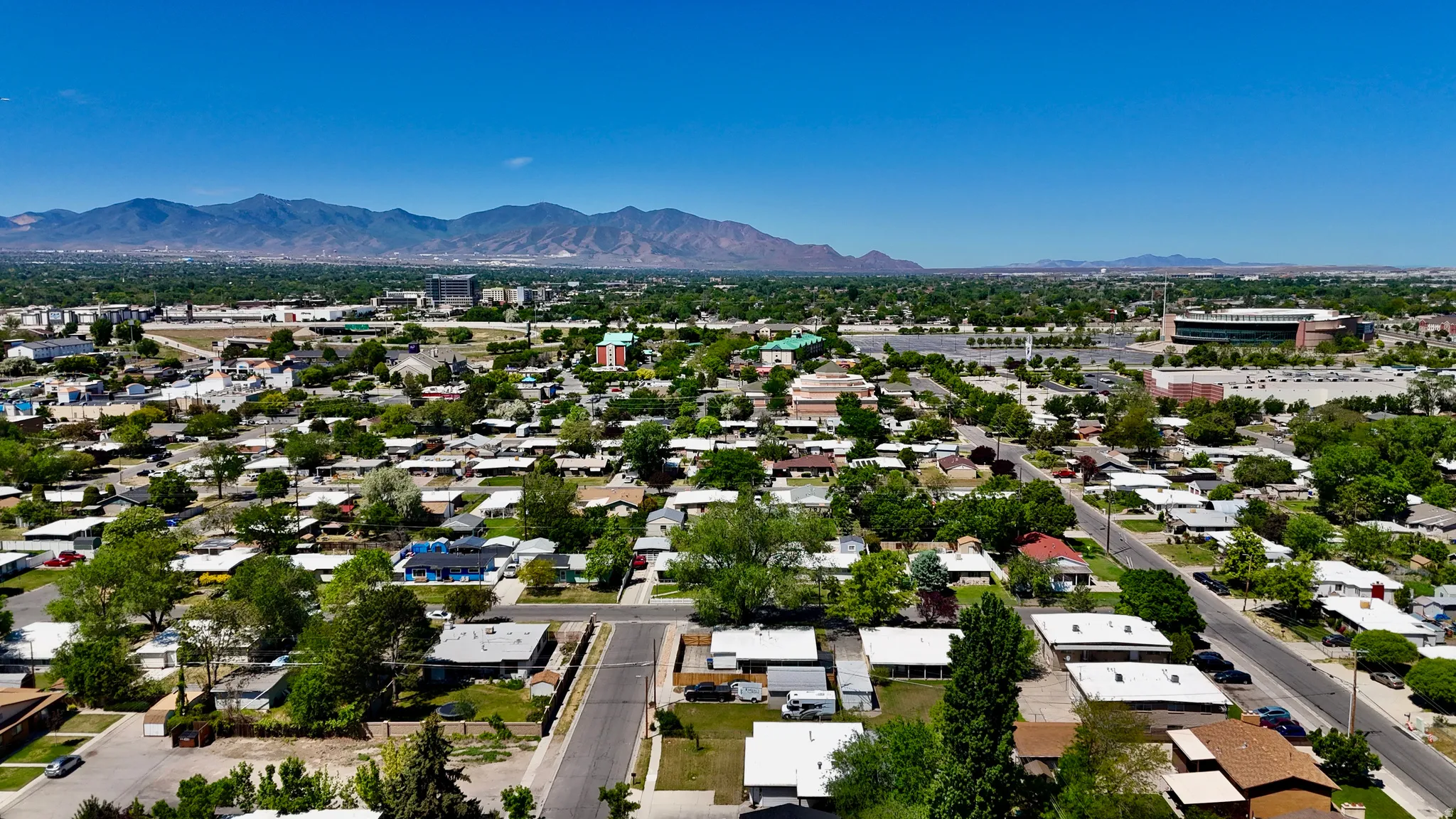 Expansive aerial perspective showcasing a neighborhood with mature trees and mountain scenery in the background