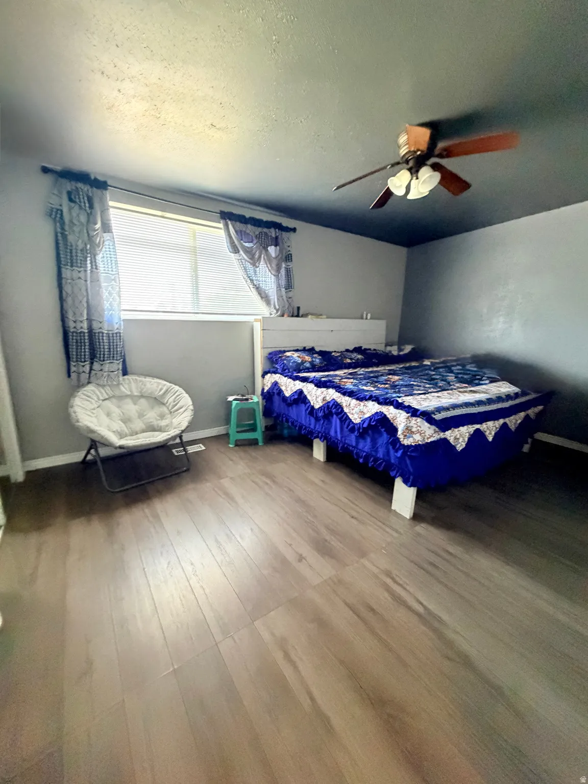 Wood-finish laminate flooring throughout, featuring a window with blinds, and a ceiling fan with integrated lighting