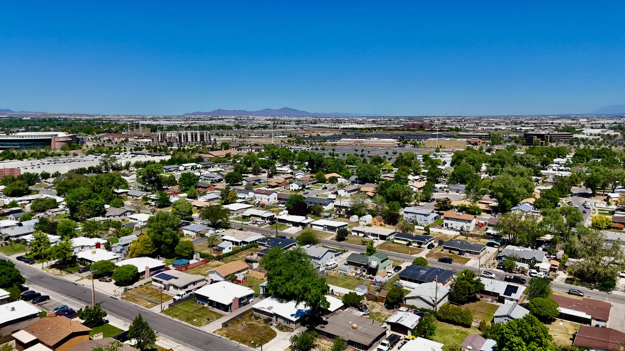 Sprawling suburban landscape featuring residential properties with mature trees, paved streets, and distant commercial structures