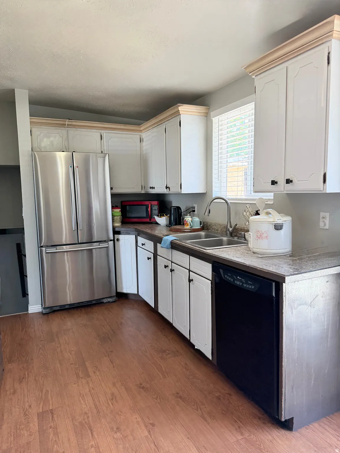 Kitchen featuring white cabinetry with natural wood crown molding, stainless steel French door refrigerator, black dishwasher, and a double basin stainless steel sink
