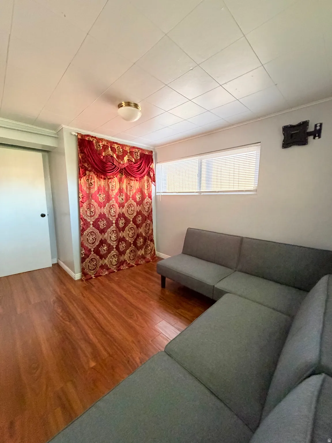 Room featuring laminate wood-finish flooring, a rectangular window with blinds, and a flush mount ceiling light