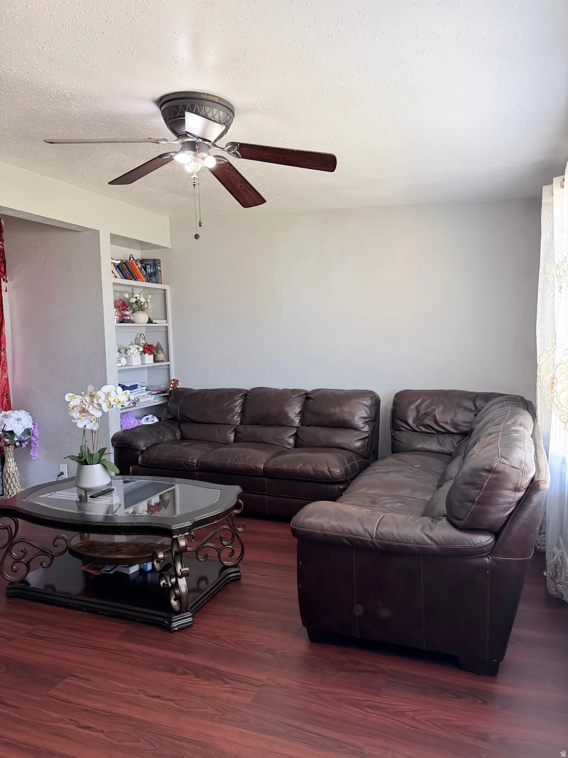 Living area featuring wood-finish flooring, a ceiling fan with integrated lighting, and a built-in shelving unit
