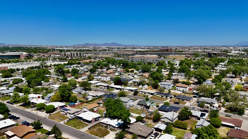 Sprawling suburban landscape featuring residential properties with mature trees, paved streets, and distant commercial structures