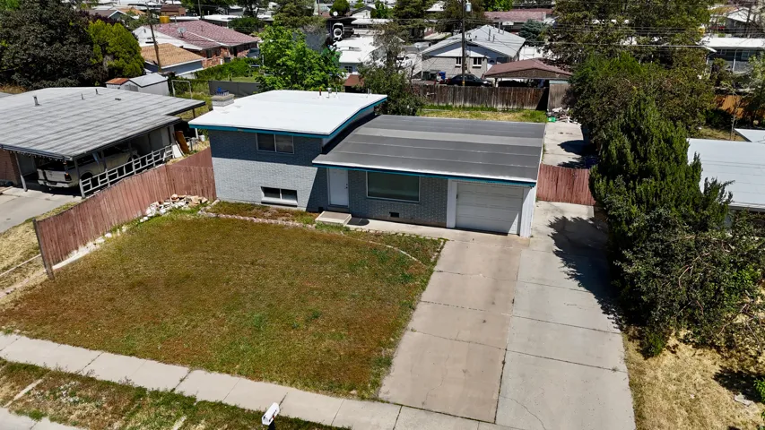 Exterior featuring a light gray facade, attached garage, concrete driveway, front lawn, and mature perimeter trees