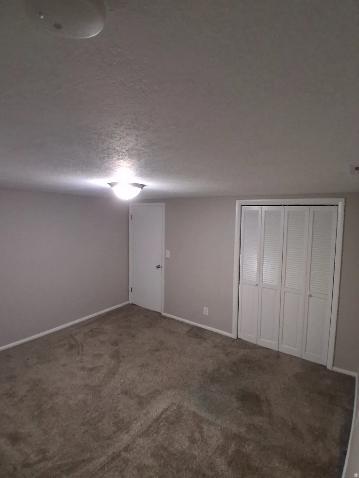 Unfurnished bedroom featuring a textured ceiling, dark carpet, and a closet