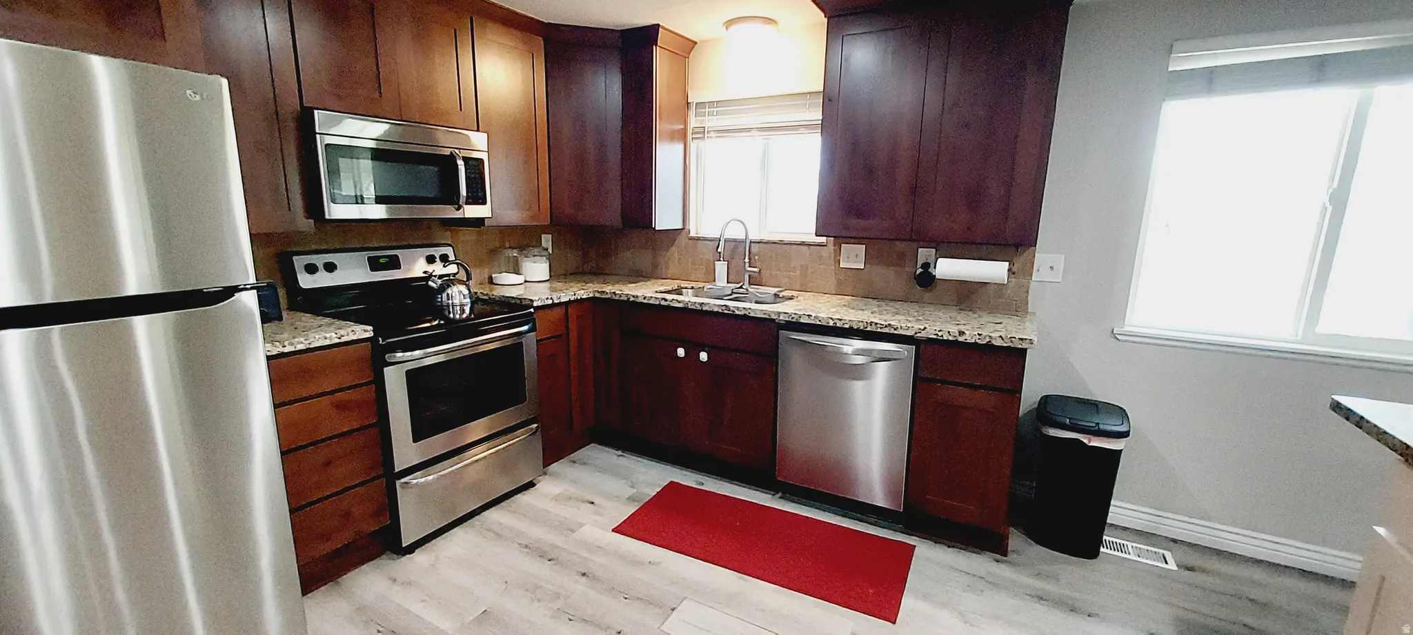 Kitchen with stainless steel appliances, light stone countertops, and decorative backsplash