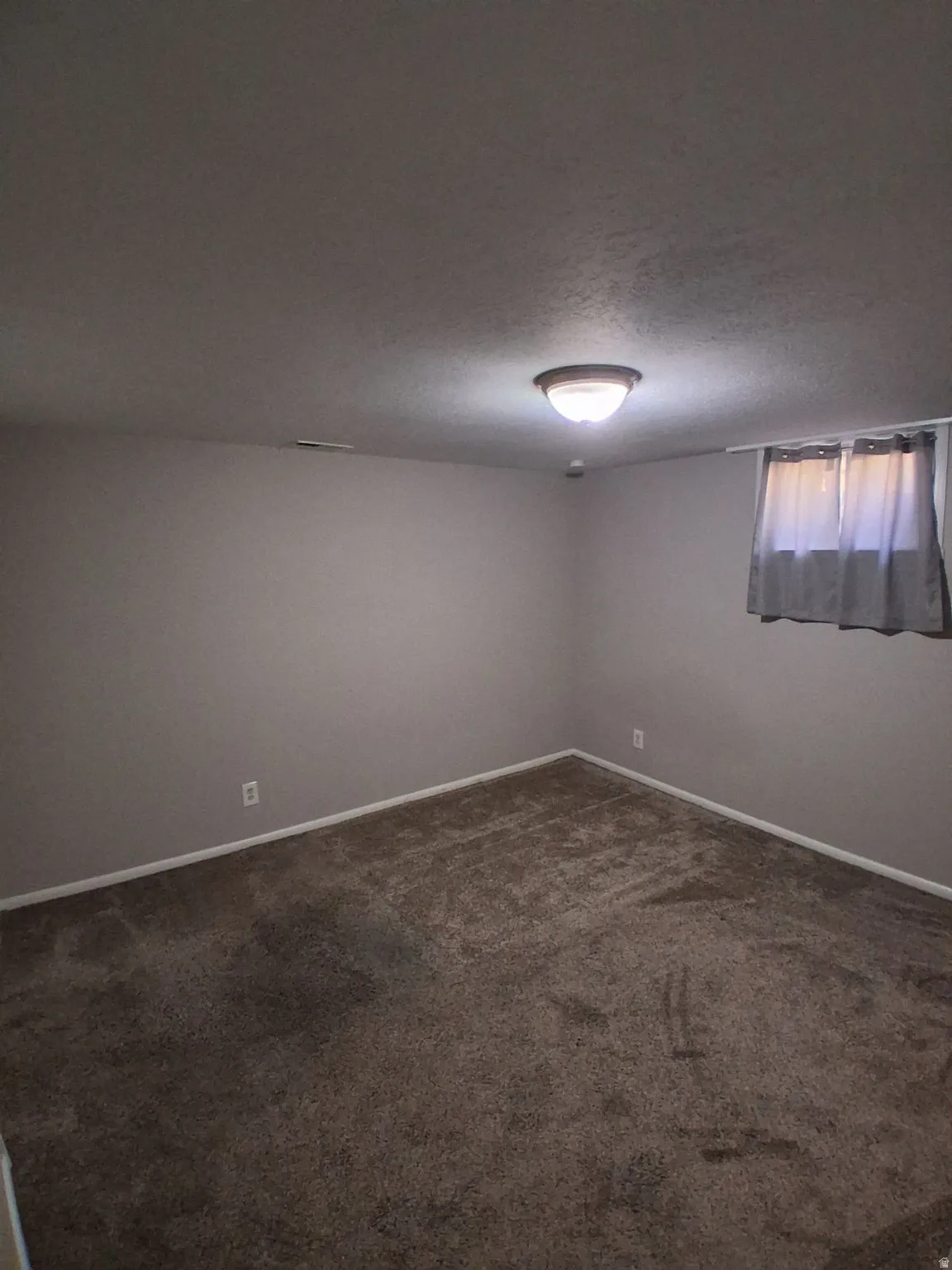 Empty room with a textured ceiling and dark colored carpet