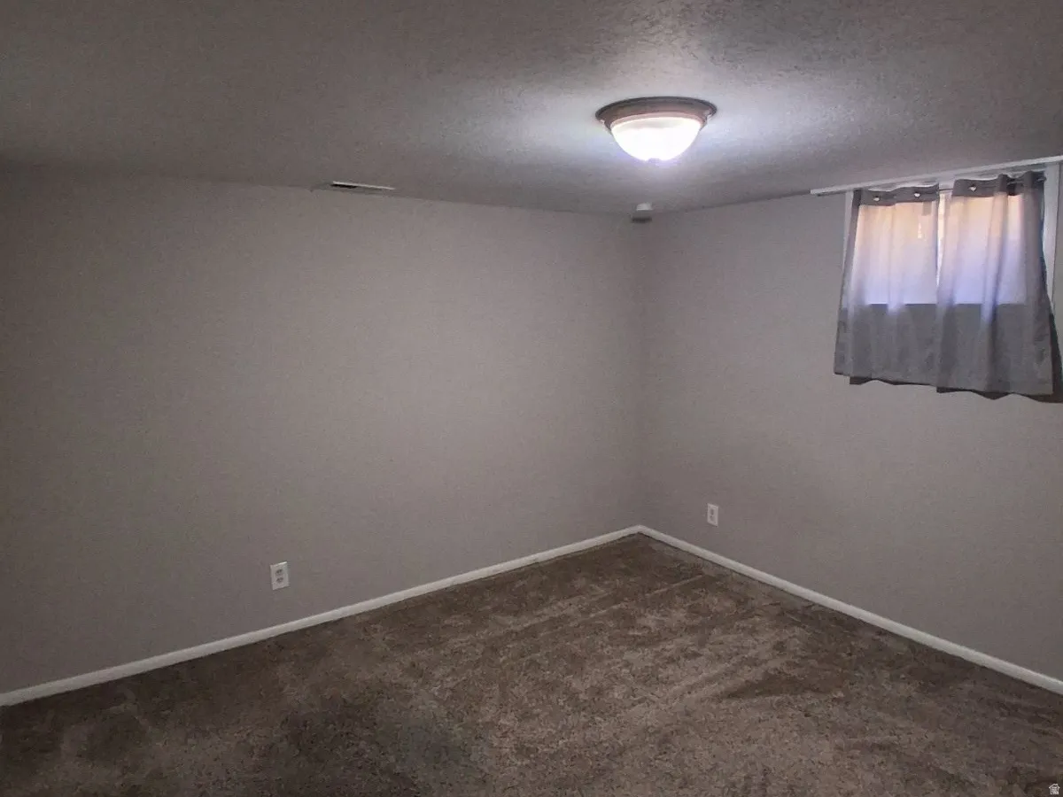 Unfurnished room featuring dark colored carpet and a textured ceiling