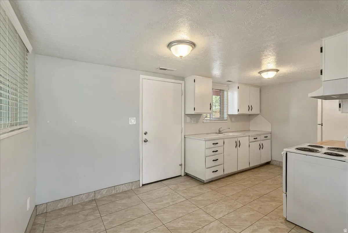 Kitchenette featuring white cabinetry with dark hardware, a single basin sink, and a white oven range with an overhead hood