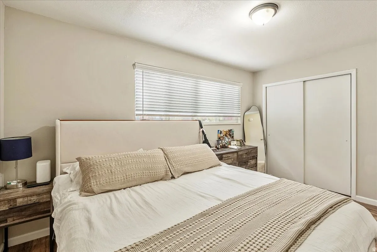 Bedroom featuring neutral wall tones, window with blinds, overhead flush mount lighting, wood-finish flooring, and sliding closet doors