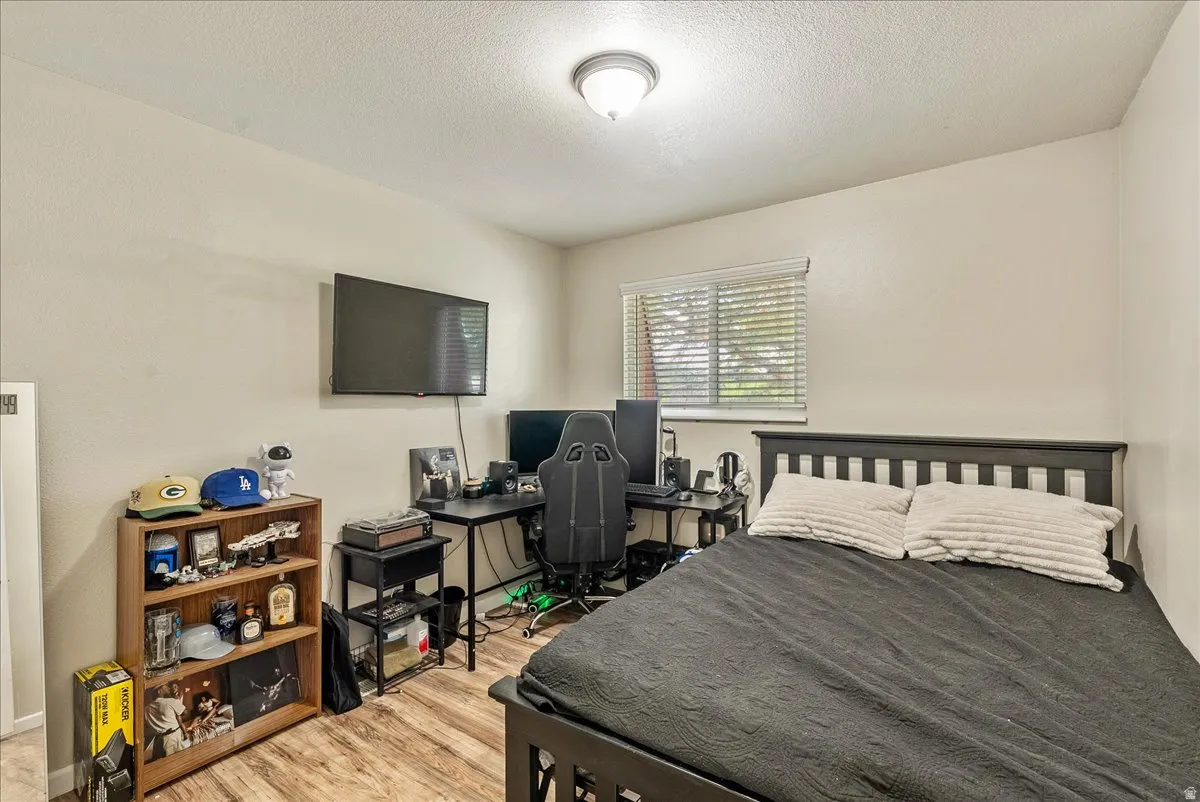 Room featuring wood-finish flooring, a ceiling-mounted light fixture, and a window with horizontal blinds