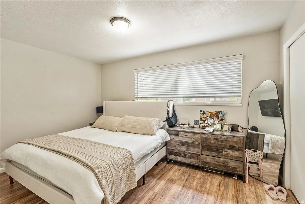 Bright room with wood-finish flooring, a window featuring horizontal blinds, and a flush-mount ceiling light fixture