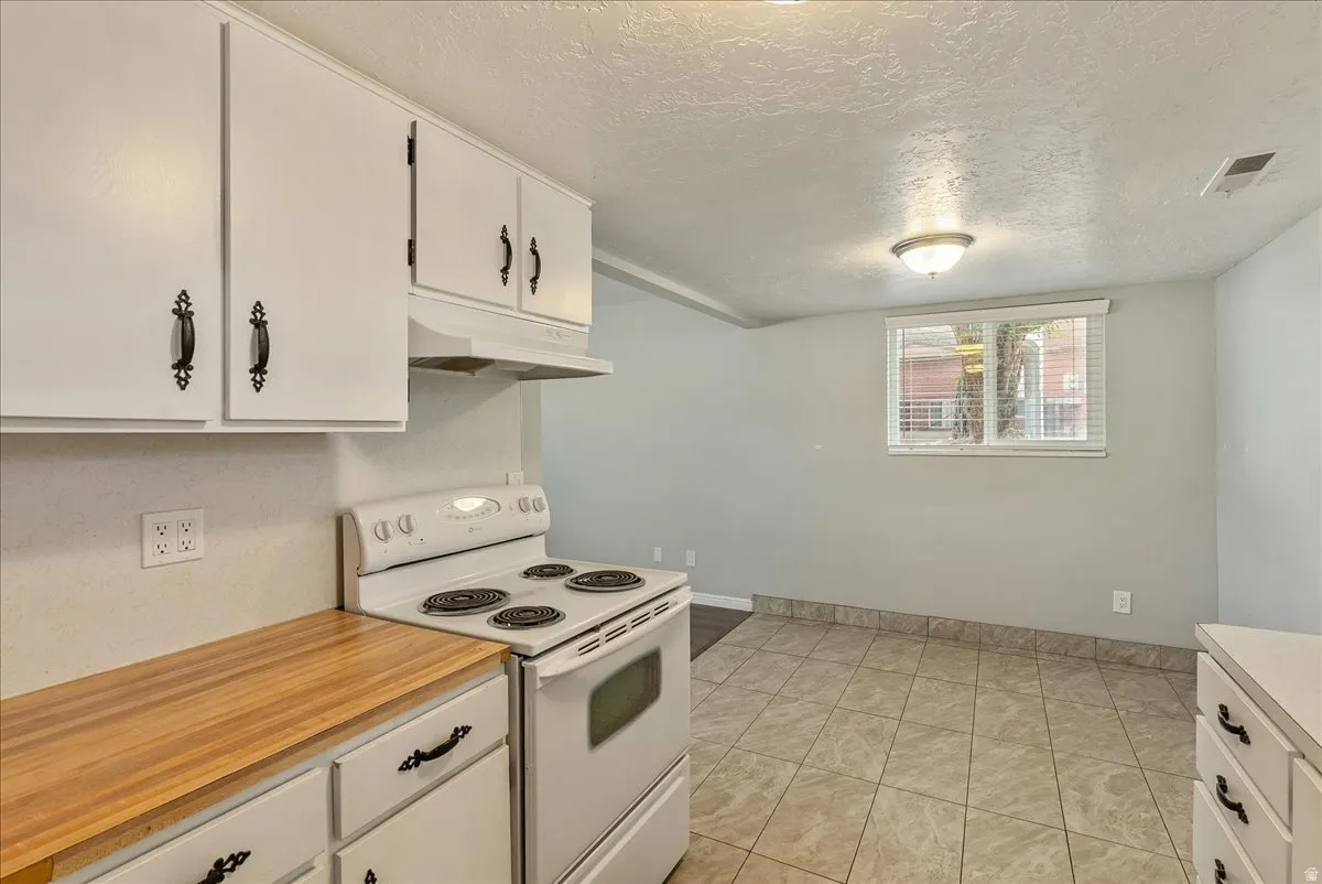 Kitchen space featuring white cabinetry, wood-finish countertops, a white range, and tiled flooring