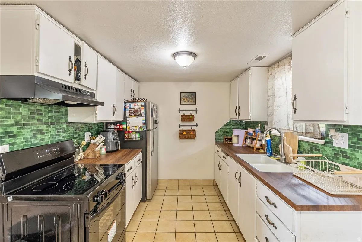Galley kitchen featuring white cabinetry, wood-finish countertops, and a green tile backsplash