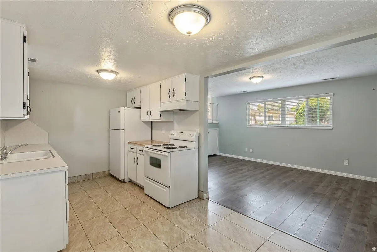 Kitchen featuring white cabinetry, a white refrigerator, a white electric range, and tile flooring