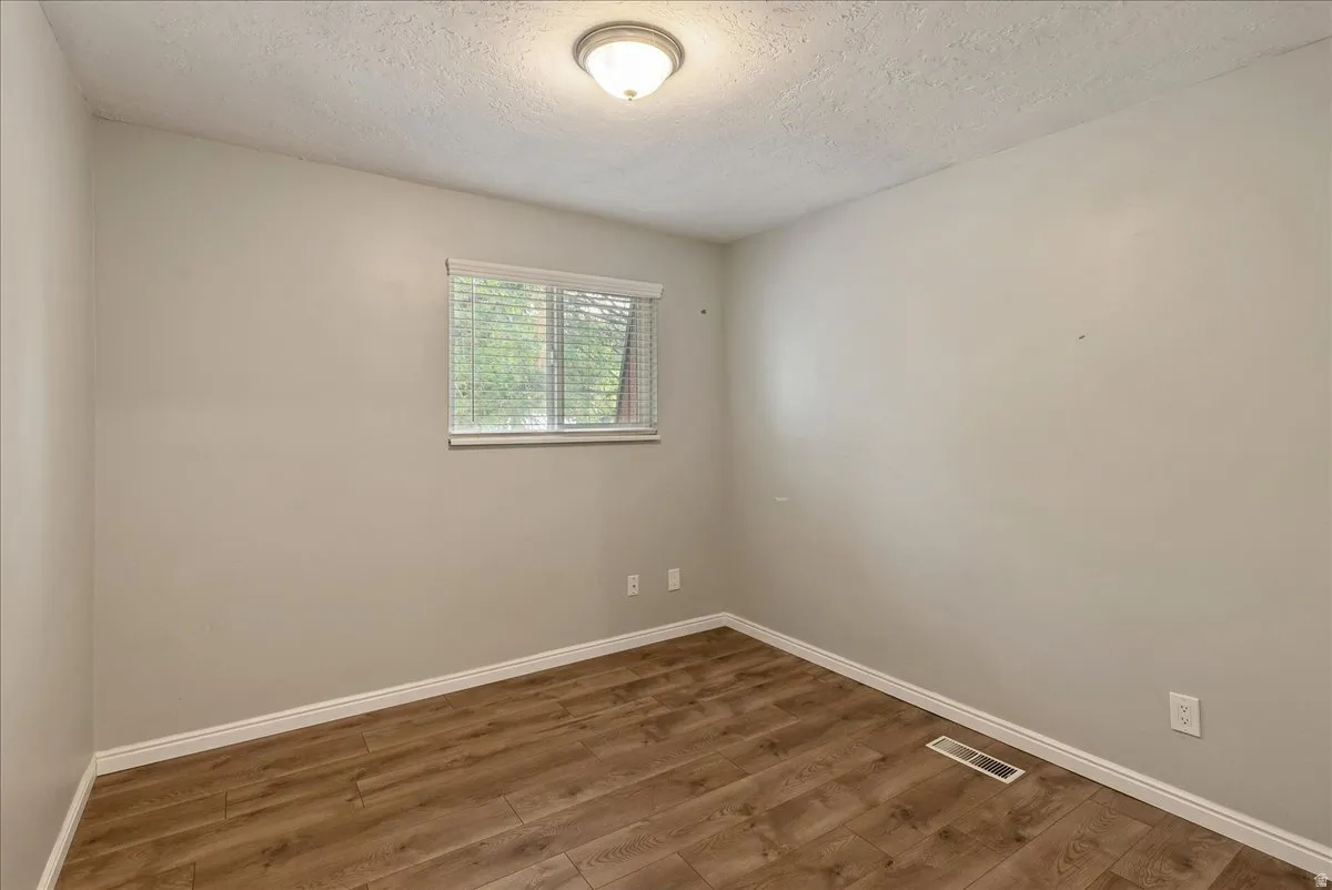 Room featuring wood-finish flooring, light gray walls, a window with blinds, and a flush-mount ceiling light
