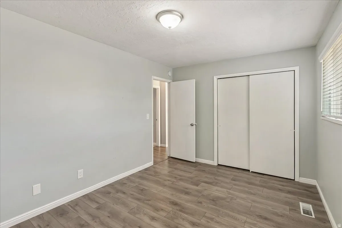 Neutral gray wall paint with white trim, wood-finish flooring, white sliding closet doors, and a window with blinds