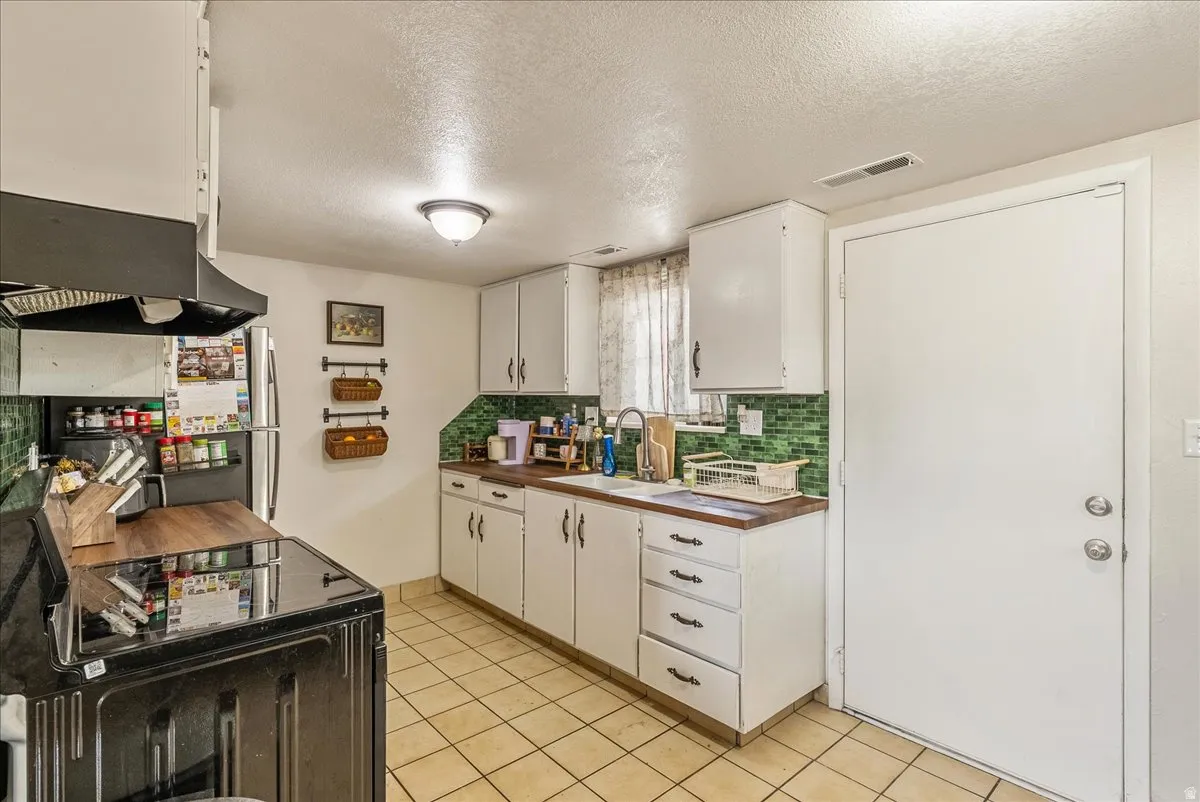 Kitchen featuring white cabinetry, wood-finish countertops, and a green tile backsplash