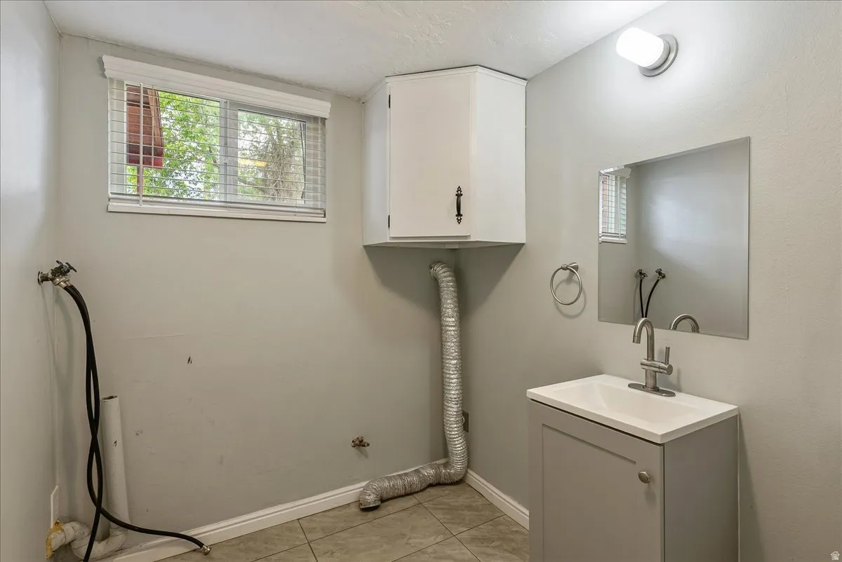 Utility space featuring a single window, white window blinds, a corner wall cabinet, a wall-mounted vanity light, and a sink with a single-handle faucet