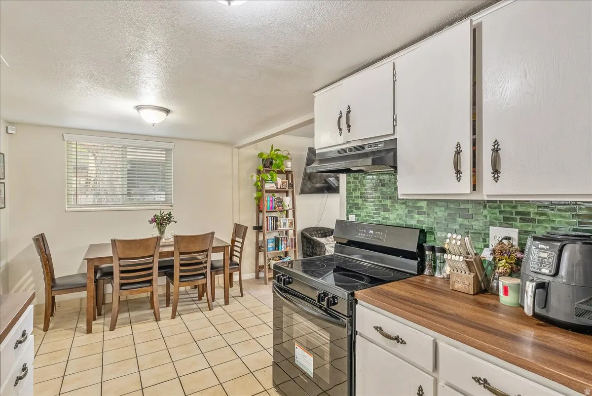 Kitchen featuring white cabinetry, wood-finish countertops, and a green tile backsplash