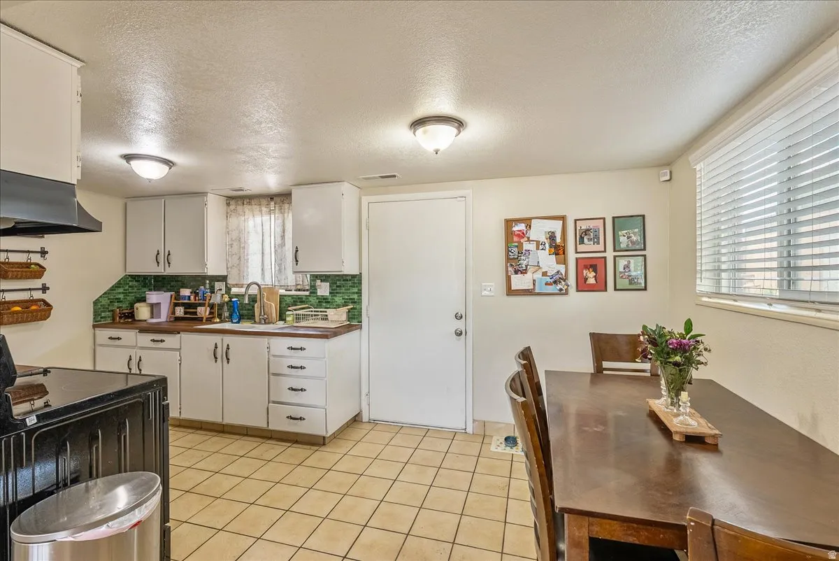 Kitchen area featuring white cabinetry, a green tiled backsplash, and wood-finish countertops