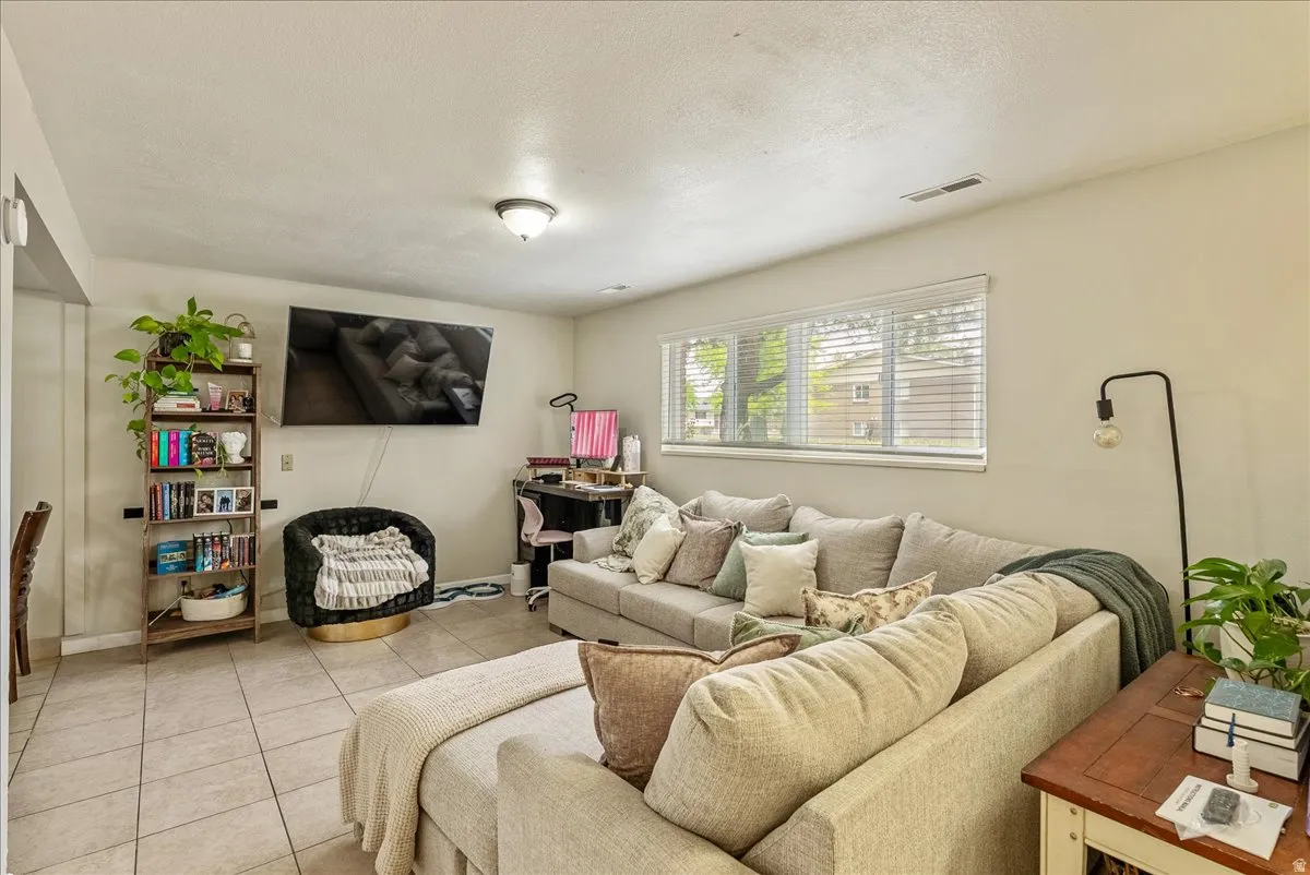 Spacious living area featuring tile flooring, neutral wall tones, and a large window with blinds
