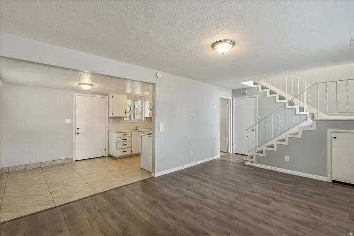 Living area featuring wood-finish flooring, a white staircase with metal railing, and a separate kitchen area with tile flooring and white cabinetry