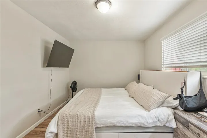 Light-filled bedroom featuring wood-finish flooring, a ceiling-mounted light fixture, and a window with horizontal blinds