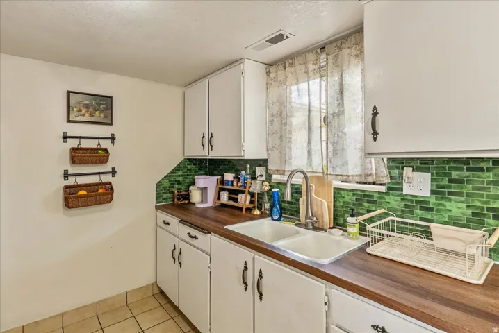 Kitchen featuring white cabinetry, a dual basin stainless steel sink, wood-finish countertops, and a vibrant green subway tile backsplash