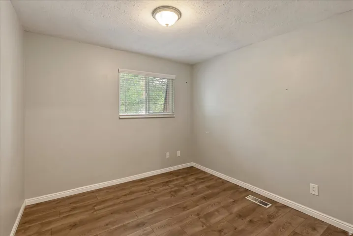 Room featuring wood-finish flooring, light gray walls, a window with blinds, and a flush-mount ceiling light