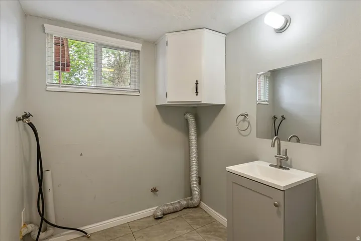 Utility space featuring a single window, white window blinds, a corner wall cabinet, a wall-mounted vanity light, and a sink with a single-handle faucet