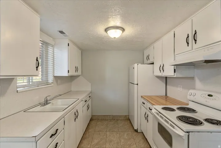 Galley-style kitchen featuring white cabinetry, a double basin sink, and a four-burner electric range with an overhead hood
