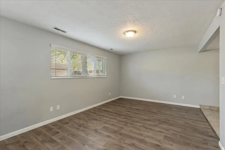 Spacious interior room featuring wood-finish flooring, light gray wall tones, a large window with blinds, and recessed ceiling lighting