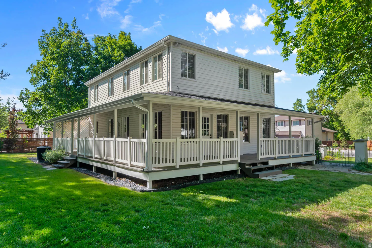 Two-story exterior with light-colored siding, a wrap-around porch, and white balustrades