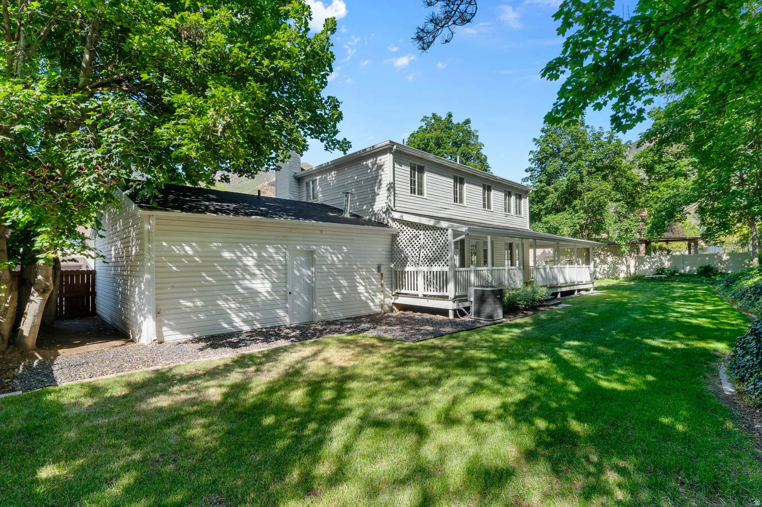 Rear exterior featuring a covered porch with white railing, light-colored siding, and a spacious green lawn
