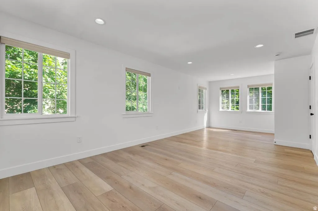 Spacious room featuring light wood-finish flooring, recessed lighting, multiple windows with white trim, and a neutral color palette