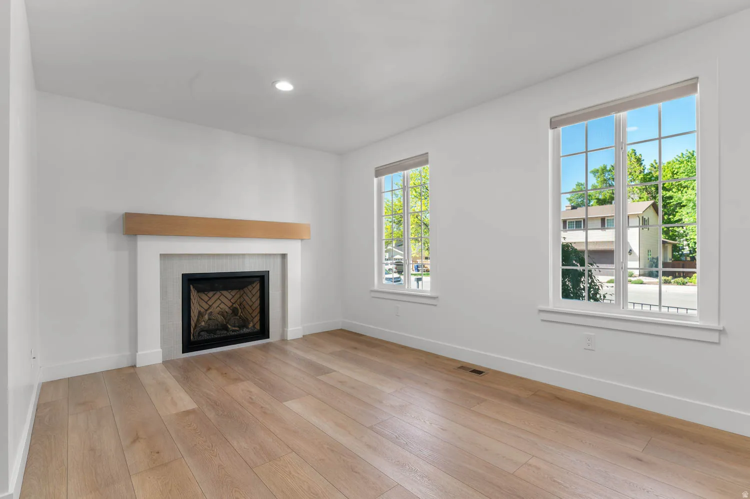 Office space featuring a white fireplace with a light wood mantel, light wood-finish flooring, two large windows, and recessed lighting